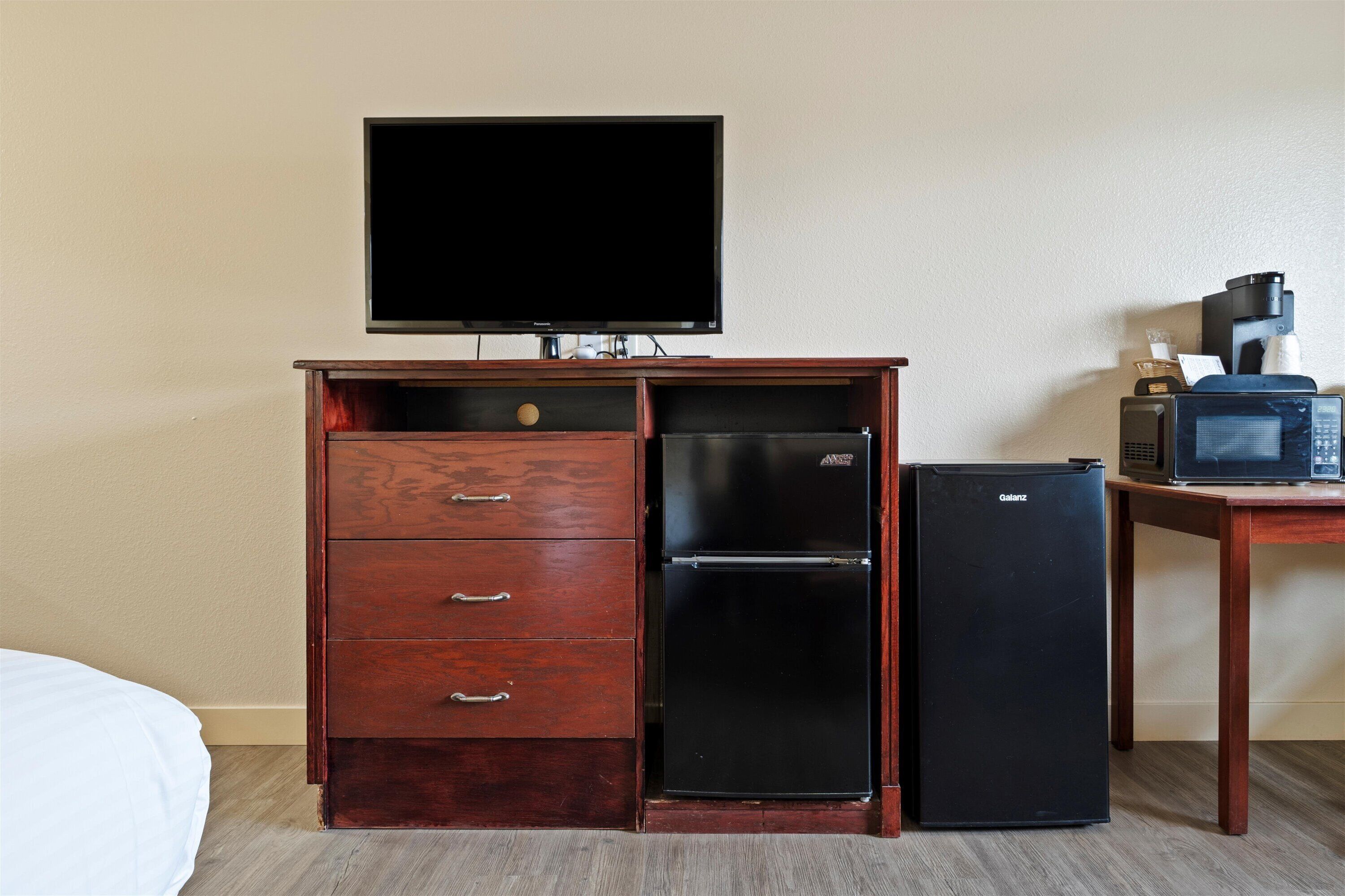 A hotel room with a wooden cabinet, a television, a black refrigerator, and a microwave.