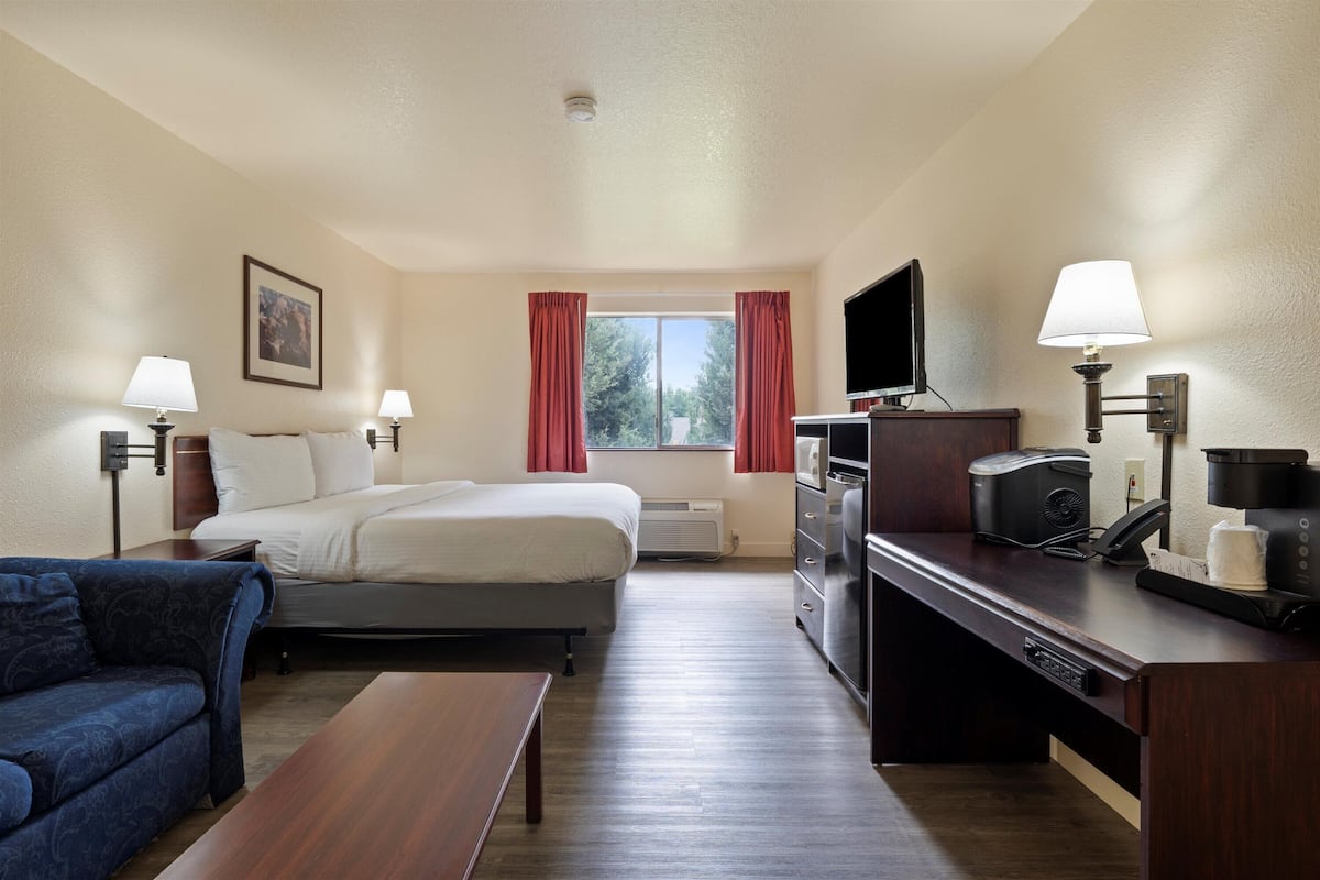 A hotel room with a bed, a desk with a computer, a TV, a coffee maker, and a couch.