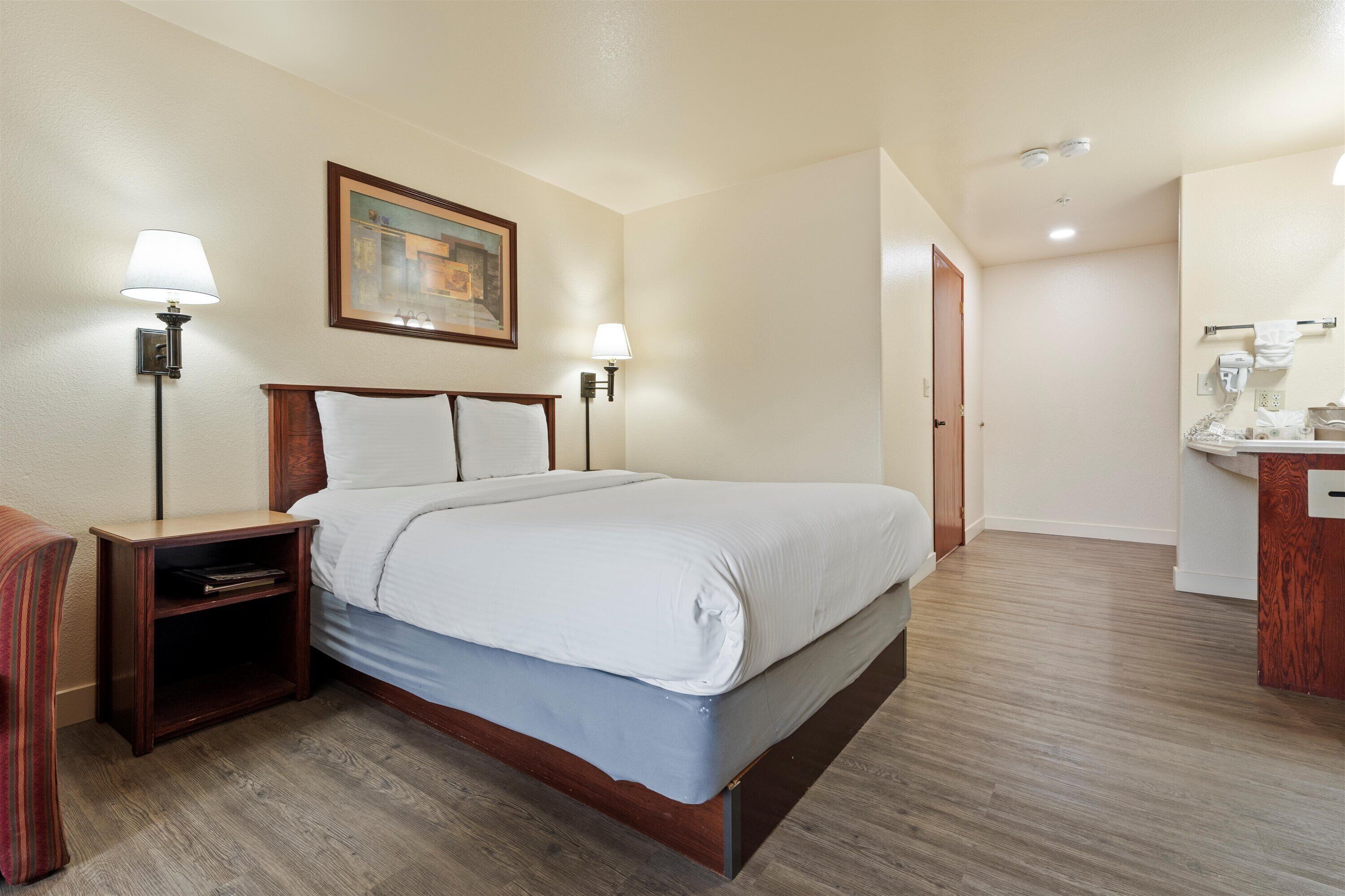 A hotel room with a bed, nightstands, a painting on the wall, and a bathroom visible through an open door.