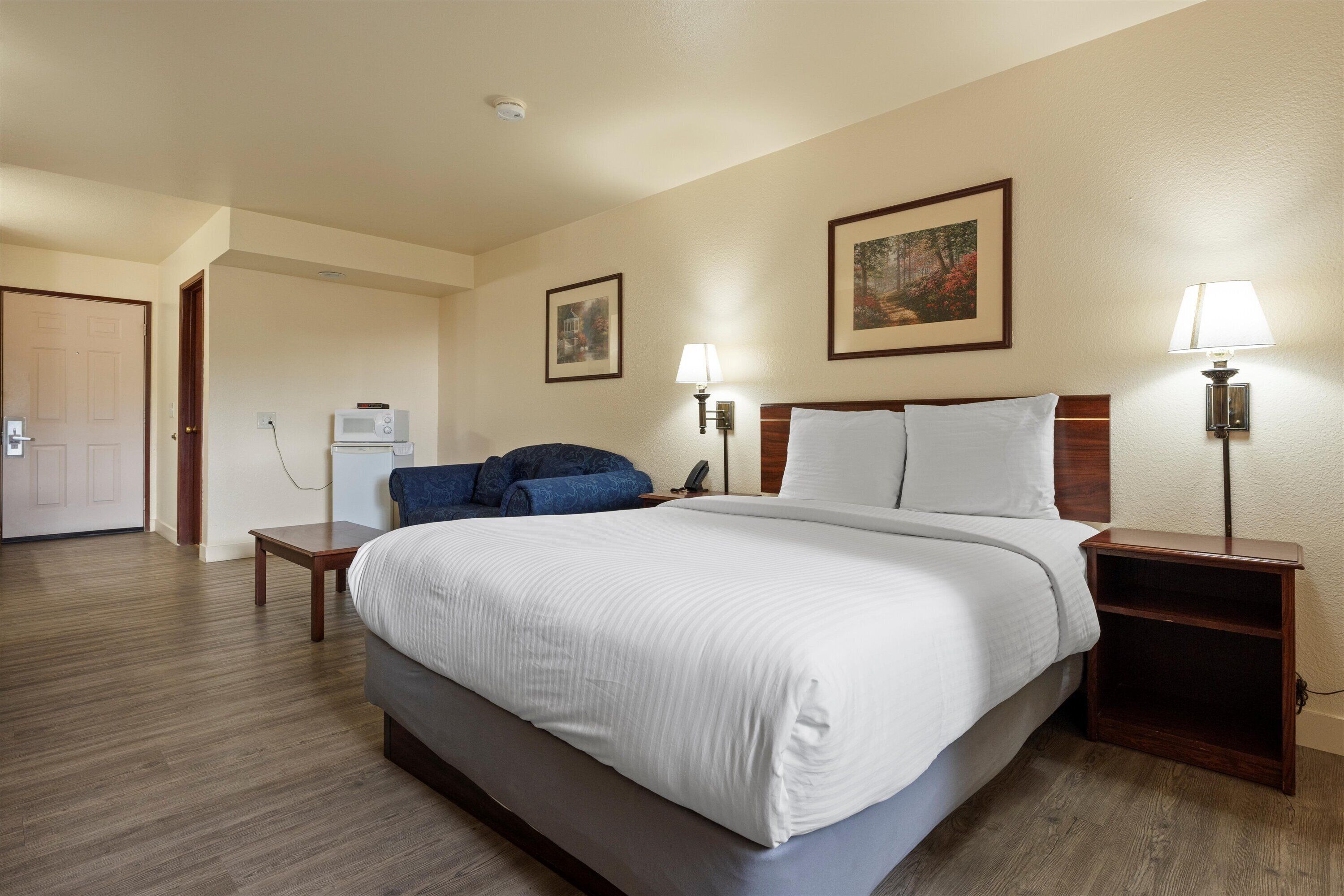 Una camera d'albergo con un letto grande, due comodini, una scrivania, un forno a microonde e due lampade a parete.