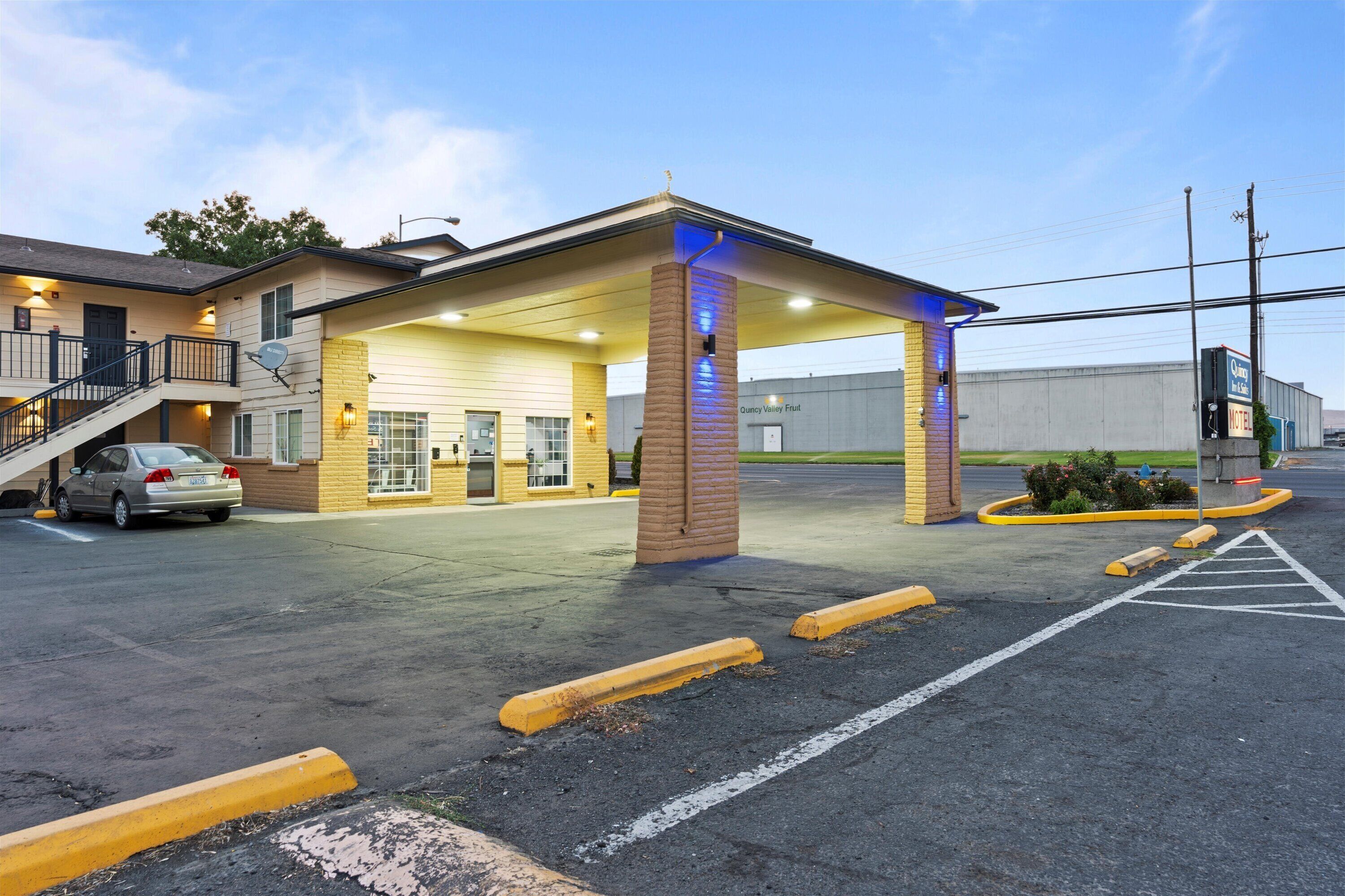 A motel with a covered parking area, a car parked inside, and a building with a sign that reads "Quincy Valley Motel."