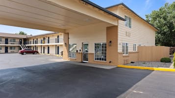 Um motel com área de estacionamento coberta, um carro vermelho estacionado dentro e uma cerca de madeira ao redor da propriedade.