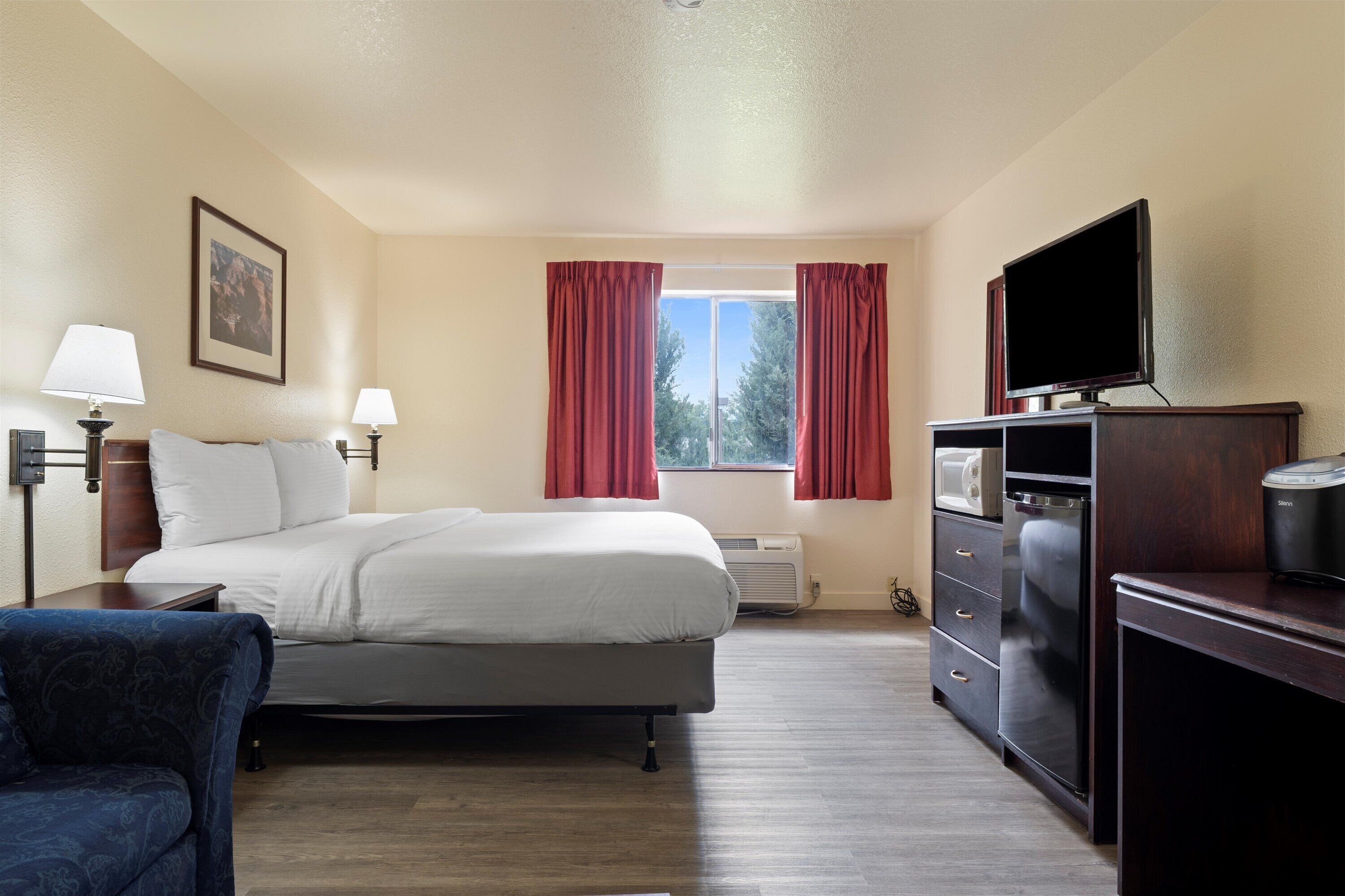 A hotel room with a bed, a desk with a television, a chair, and a window with curtains.