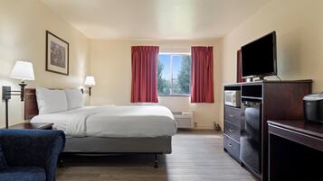 A hotel room with a bed, a desk with a television, a chair, and a window with curtains.