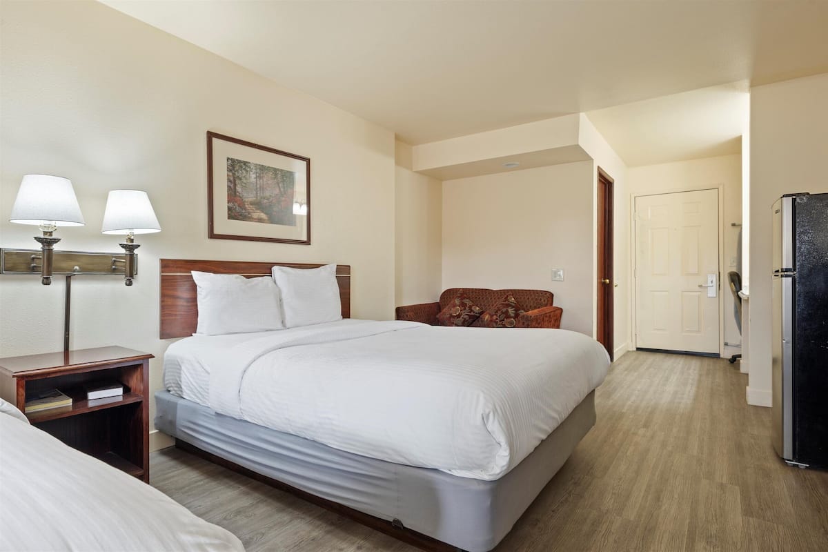 A hotel room with a large bed, two bedside tables, a nightstand, a sofa, a painting on the wall, and a door leading to another room.