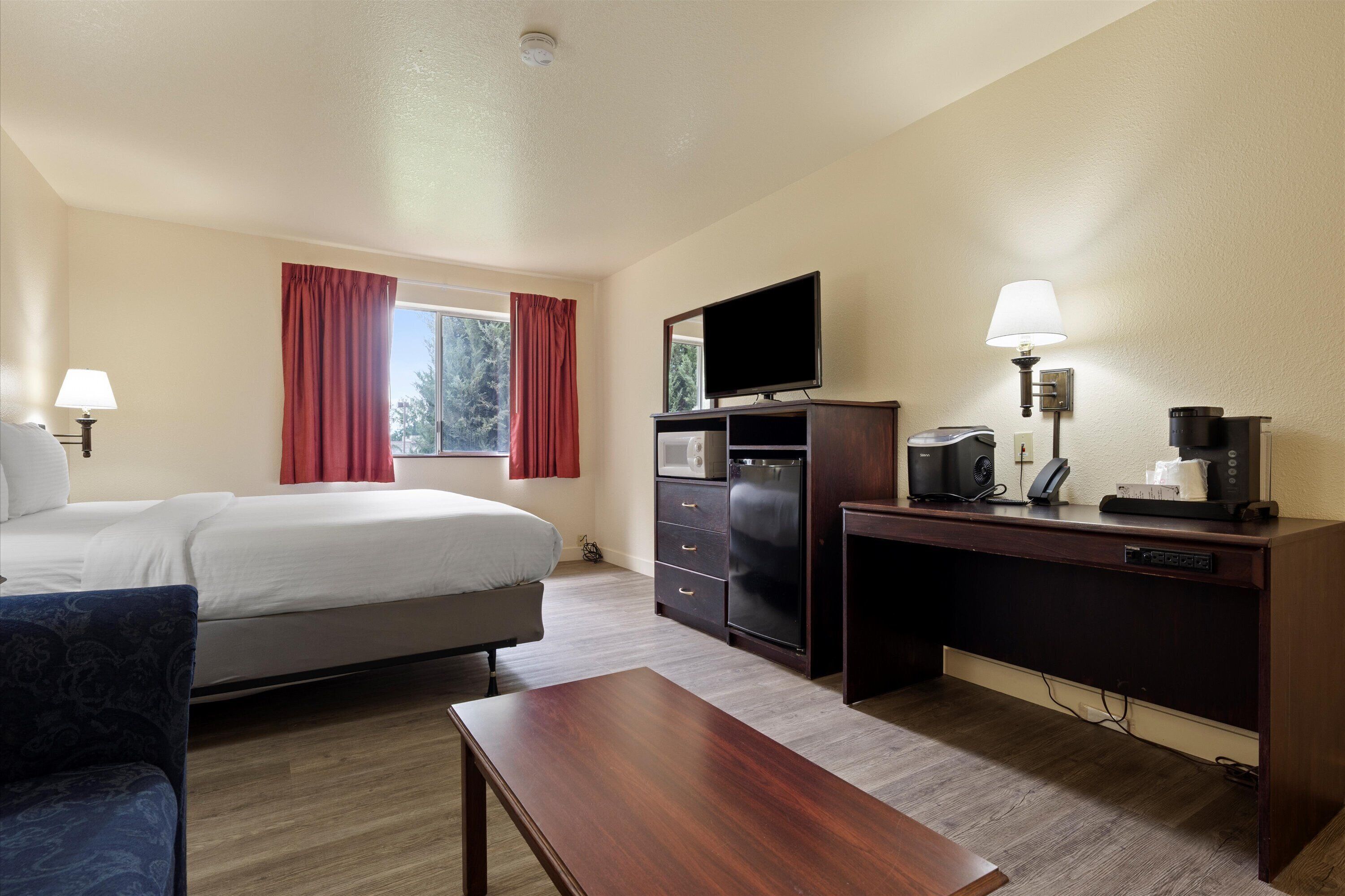 Ein Hotelzimmer mit Bett, Schreibtisch, Fernseher, Kaffeemaschine und Lampe.