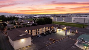 A motel with a parking lot, a gas station, and a large building in the background. - Quincy INN and Suites (Quincy)
