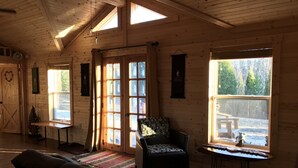 En mysig stuga med träpanel i taket, stora fönster, en soffa, en fåtölj och ett litet bord.