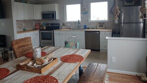 A modern kitchen with white cabinets, a stainless steel refrigerator, and a wooden dining table with orange coasters.