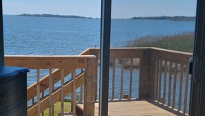 A room with a large sliding glass door leading to a wooden deck overlooking a body of water.