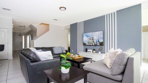 Ein modernes Wohnzimmer mit grauem Sofa, schwarzem Sofa, Couchtisch mit Pflanze und Fernseher an der Wand.