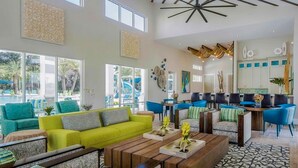 Ein geräumiger Wohnbereich mit einem leuchtend grünen Sofa, einem Holztisch und blauen Stühlen. Es gibt eine Küchenzeile mit weißen Schränken und blauen Stühlen.