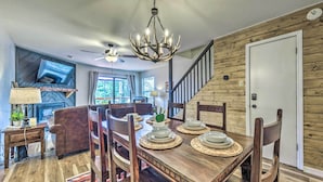 A dining area with a wooden table set for four, surrounded by chairs, a chandelier, and a television mounted on the wall. - Rustic Ruidoso Retreat Near Shops & Mountains! (Ruidoso)