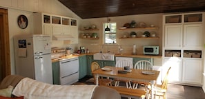 Una cocina acogedora con comedor, muebles blancos, un refrigerador, una estufa y un microondas.