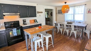Una cocina con armarios oscuros, una isla de madera y taburetes blancos.
