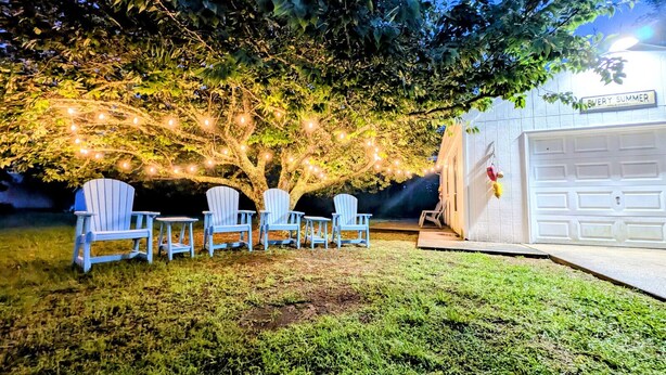 Un patio trasero con cuatro sillas Adirondack, una guirnalda de luces y un garaje con la leyenda 'EVERY SUMMER'.