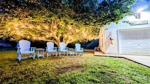 Un jardin avec quatre chaises Adirondack, une guirlande lumineuse et un garage sur lequel on peut lire : « TOUS LES ÉTÉS ».
