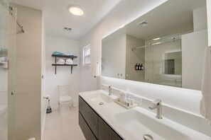 Een moderne badkamer met een grote spiegel, twee wasbakken, een douche en een toilet.
