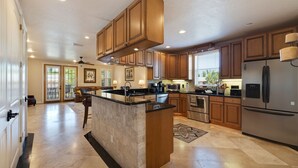 A spacious kitchen with wooden cabinets, a central island, stainless steel appliances, and a view to the living area.