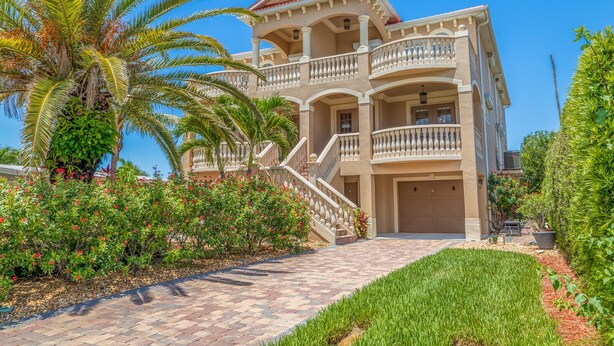 A large, multi-story building with a central staircase, balconies, and a well-maintained garden with palm trees and flowering plants.