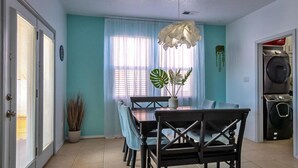 A dining area with a table, chairs, a potted plant, and a window with curtains. - O'Keeffe Paints, XL room with lock for Balloon Fiesta! (Rio Rancho)