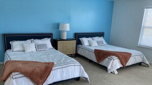 A bedroom with two beds, a nightstand, a lamp, and a window with blinds. - O'Keeffe Paints, XL room with lock for Balloon Fiesta! (Rio Rancho)