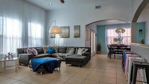 A modern living room with a sectional sofa, a dining area with a table and chairs, and a kitchen visible through an archway. - O'Keeffe Paints, XL room with lock for Balloon Fiesta! (Rio Rancho)
