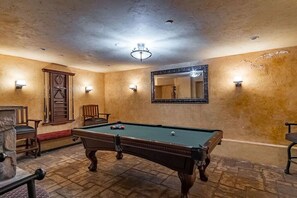 A pool table in a room with a stone fireplace, wooden chairs, and wall sconces. - KING SUITE MINS MONTEREY CARMEL (Salinas)