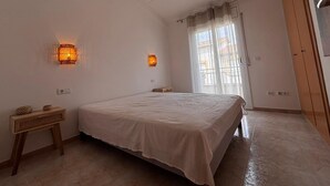 A bedroom with a bed, two wall-mounted lamps, a ceiling fan, a window with curtains, and a wooden door. - Casa Florence - L'Estartit, Els Salats (Estartit (L´))