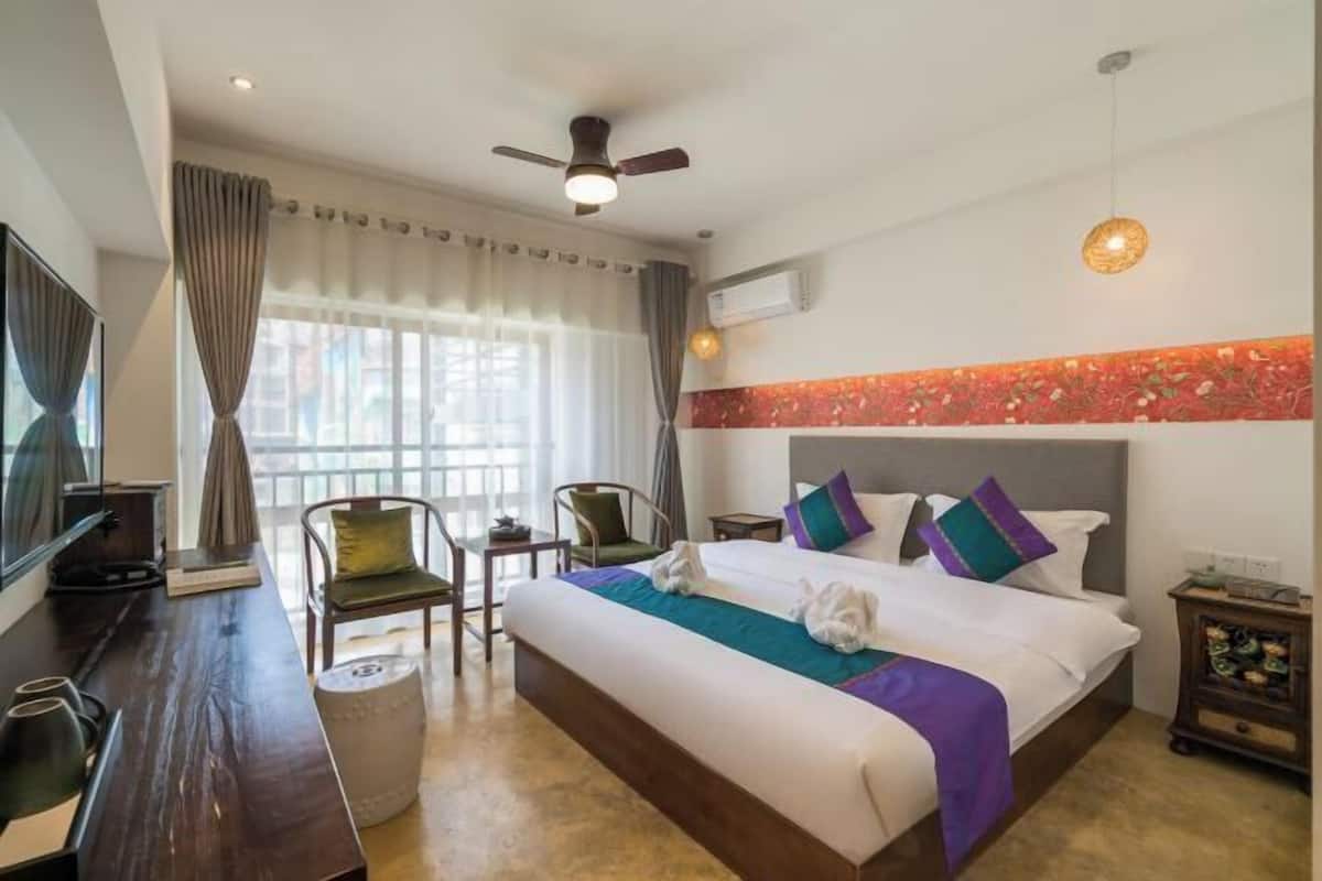 A hotel room with a bed, a desk, a chair, a TV, and a ceiling fan.