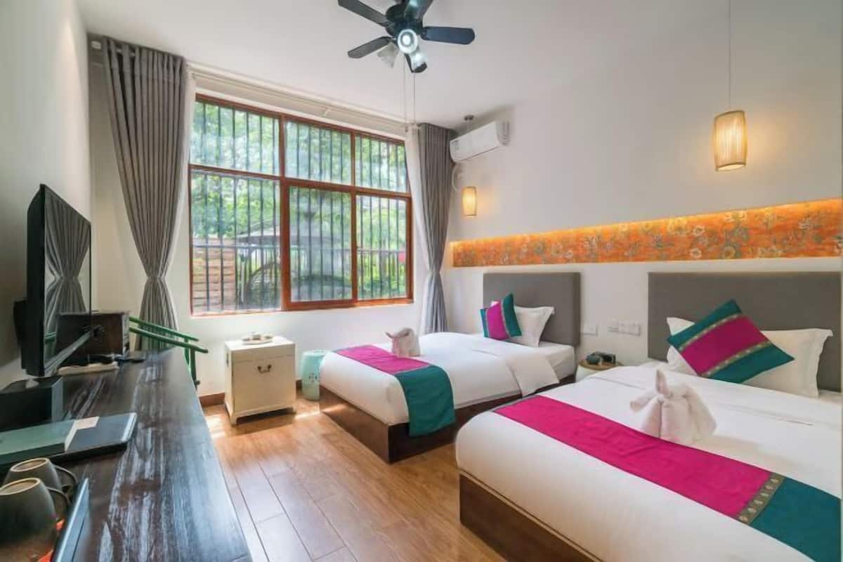 A hotel room with two beds, a desk, a TV, and a window with curtains.