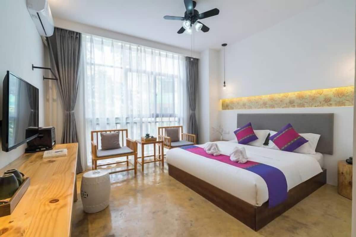 A hotel room with a bed, a desk, a chair, a television, and a ceiling fan.