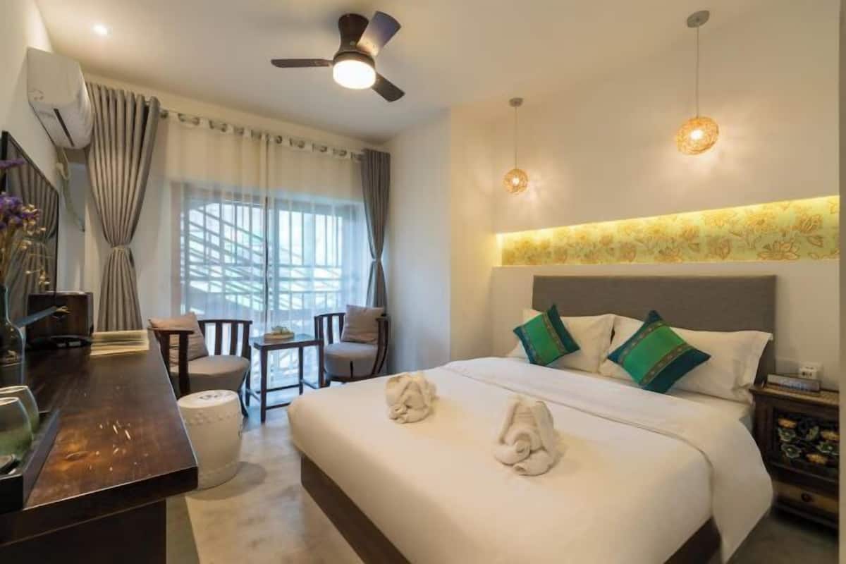 A hotel room with a bed, a desk, a chair, a ceiling fan, and a window with curtains.