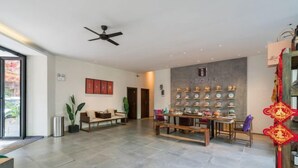 A spacious living area with a modern design, featuring a central seating area, a display of decorative items on the wall, and a ceiling fan. - Manya Hotel (Menghai)
