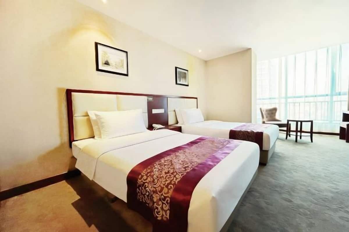 Habitación de hotel con dos camas, un escritorio, una silla y ventanas amplias.