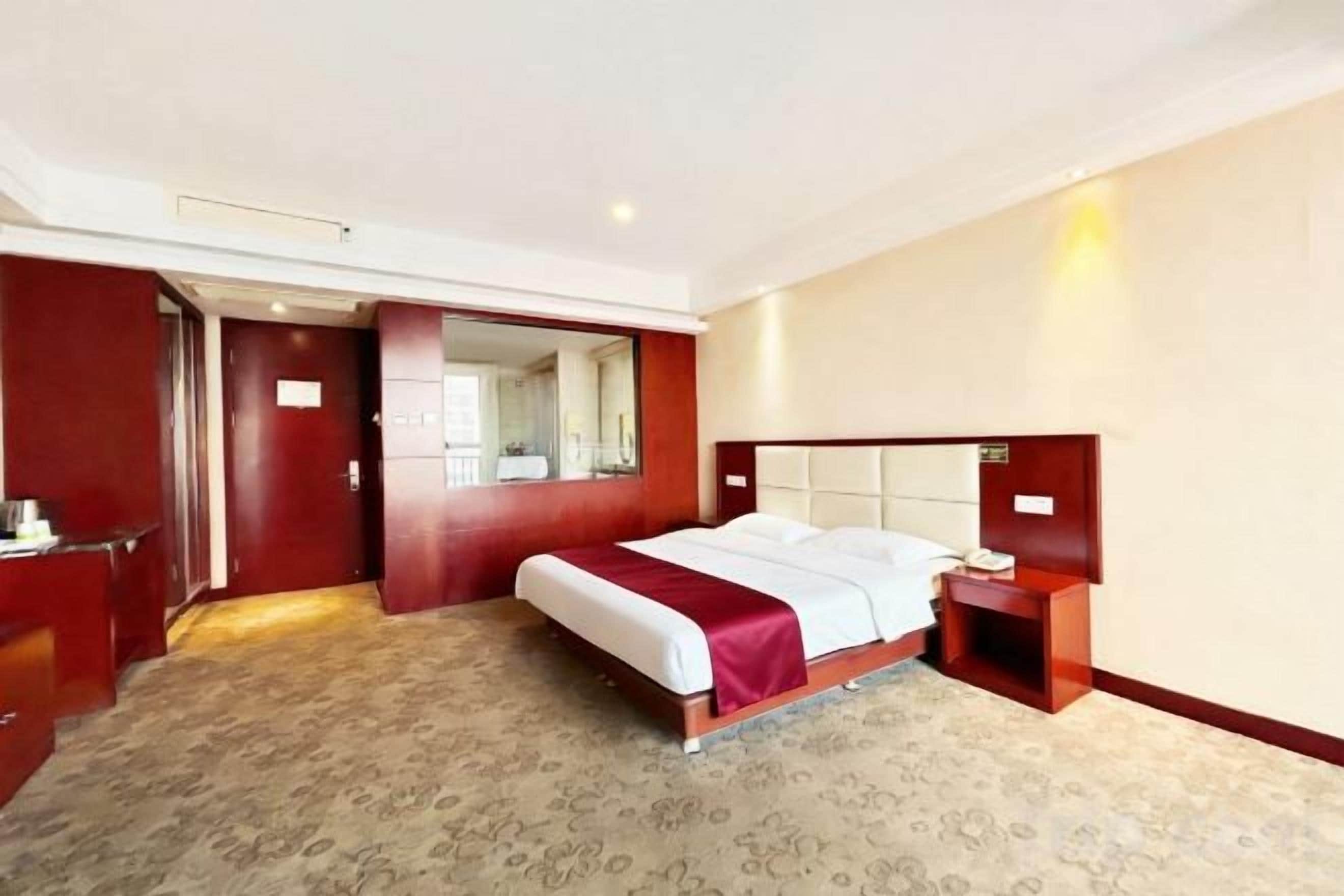 A hotel room with a bed, bedside table, and a mirror.