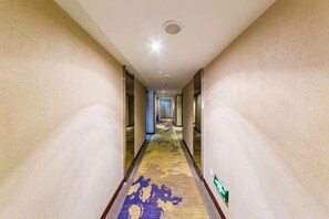 Un corridoio d'hotel con pavimento rivestito di moquette e pareti, che conduce a una camera.