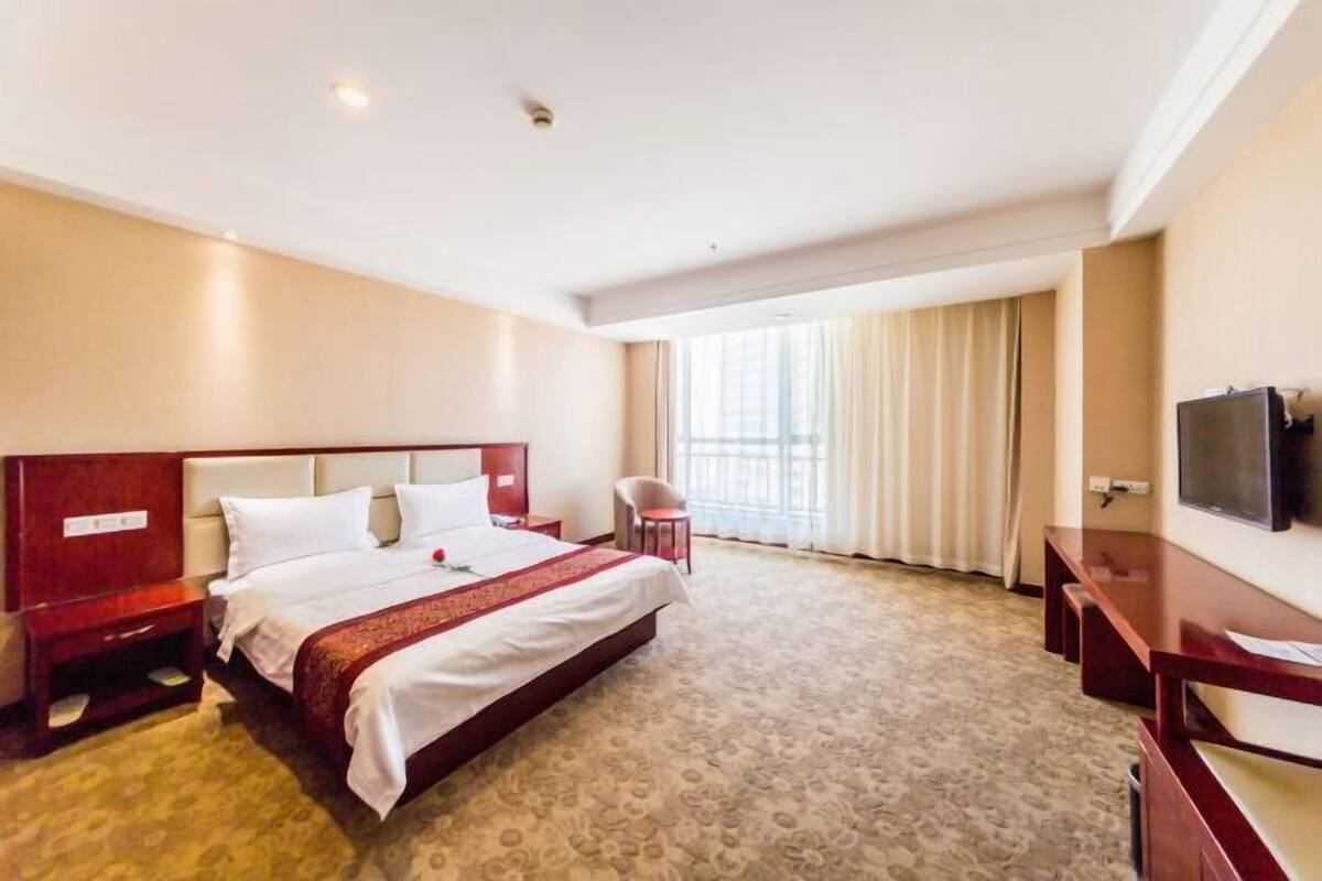 Habitación de hotel con una cama grande, un escritorio, una silla, un televisor y una ventana con cortinas.