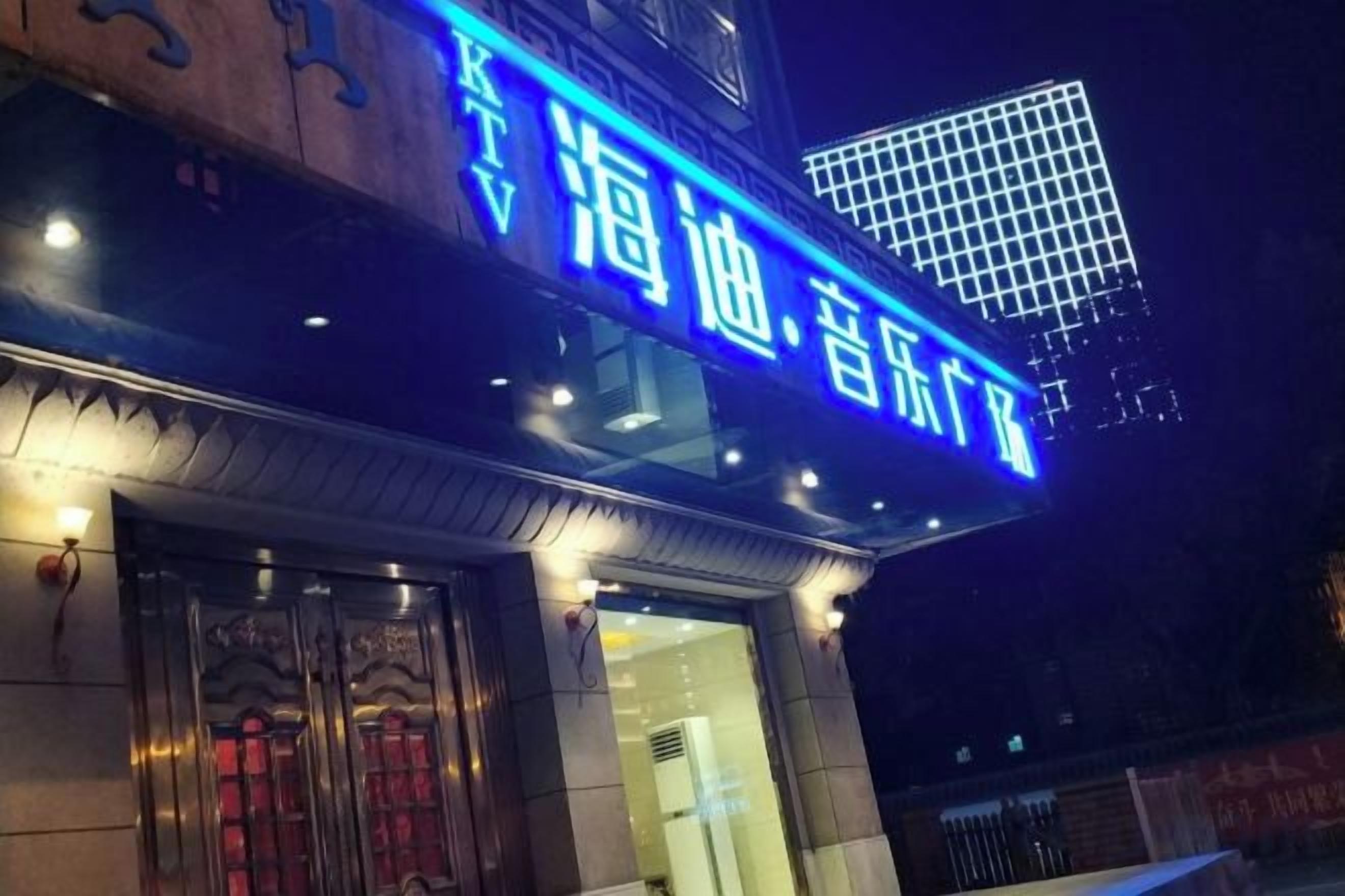 Ein Gebäude mit auffälligem, blauem Schild mit chinesischen Schriftzeichen, einem traditionellen Eingang mit aufwendigen Türen und einer modernen Glasfassade.