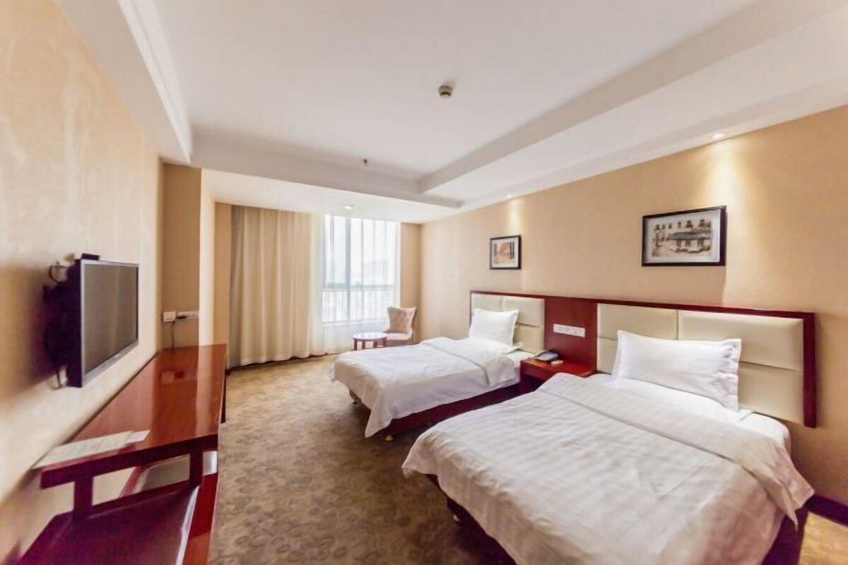 A hotel room with two beds, a TV, a desk, and a window with curtains.