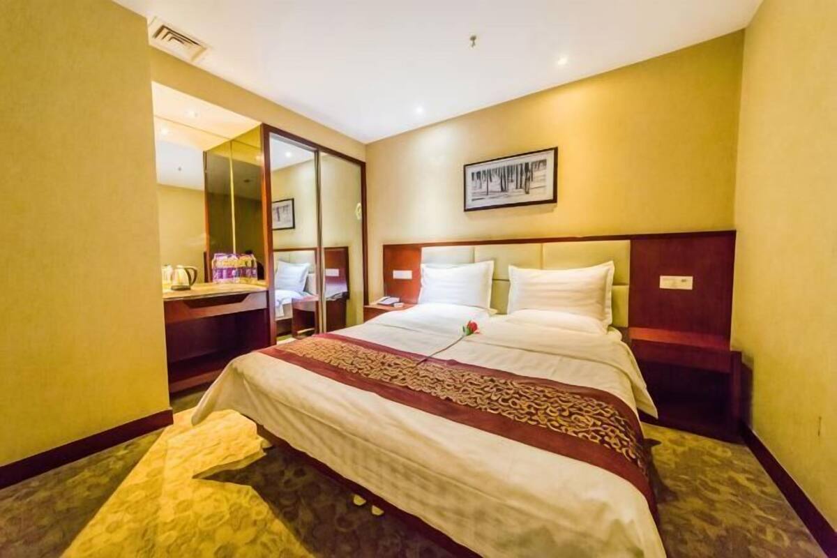 Habitación de hotel con una cama grande, un escritorio con silla, un espejo y un cuadro en la pared.