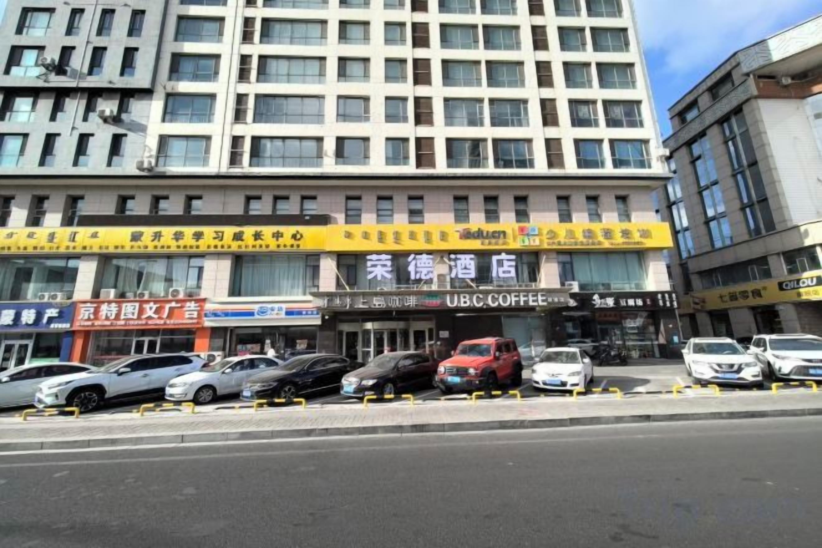 A hotel with multiple floors, a parking lot with several cars, and various storefronts including a coffee shop.