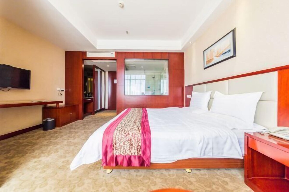 A hotel room with a large bed, a TV mounted on the wall, a desk, and a mirror.