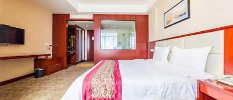 A hotel room with a large bed, a TV mounted on the wall, a desk, and a mirror.