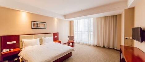 A hotel room with a large bed, a desk, a chair, a TV, and a window with curtains.