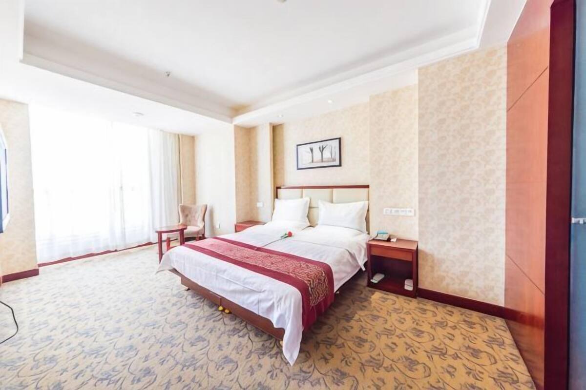Una habitación de hotel con una cama grande, una mesita de noche, una silla y un televisor.