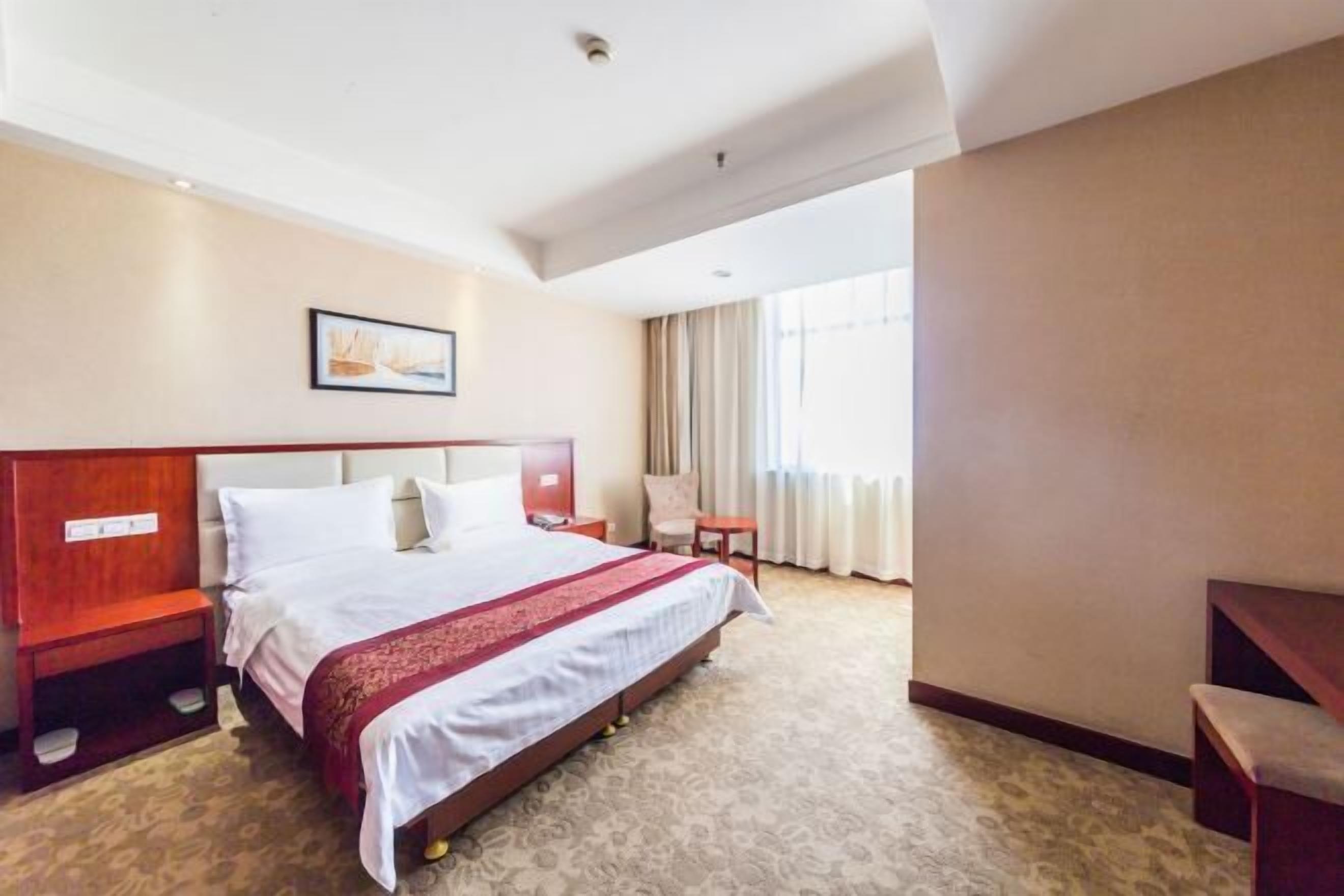 A hotel room with a large bed, a nightstand, a chair, a desk, and a window with curtains.