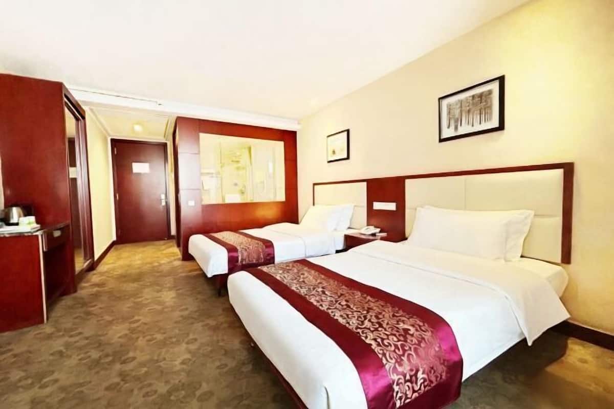 Habitación de hotel con dos camas, un escritorio, una silla y una puerta que da a otra habitación.