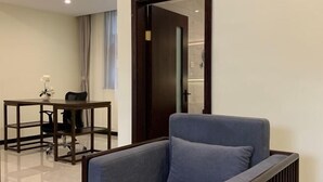 Una habitación moderna con un sillón gris, una mesa de madera con una silla, y una puerta que da a otra habitación.