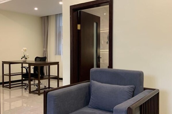 A modern room with a grey sofa, a wooden table with a chair, and a door leading to another room. - Qi Ting Hotel (Linquan)